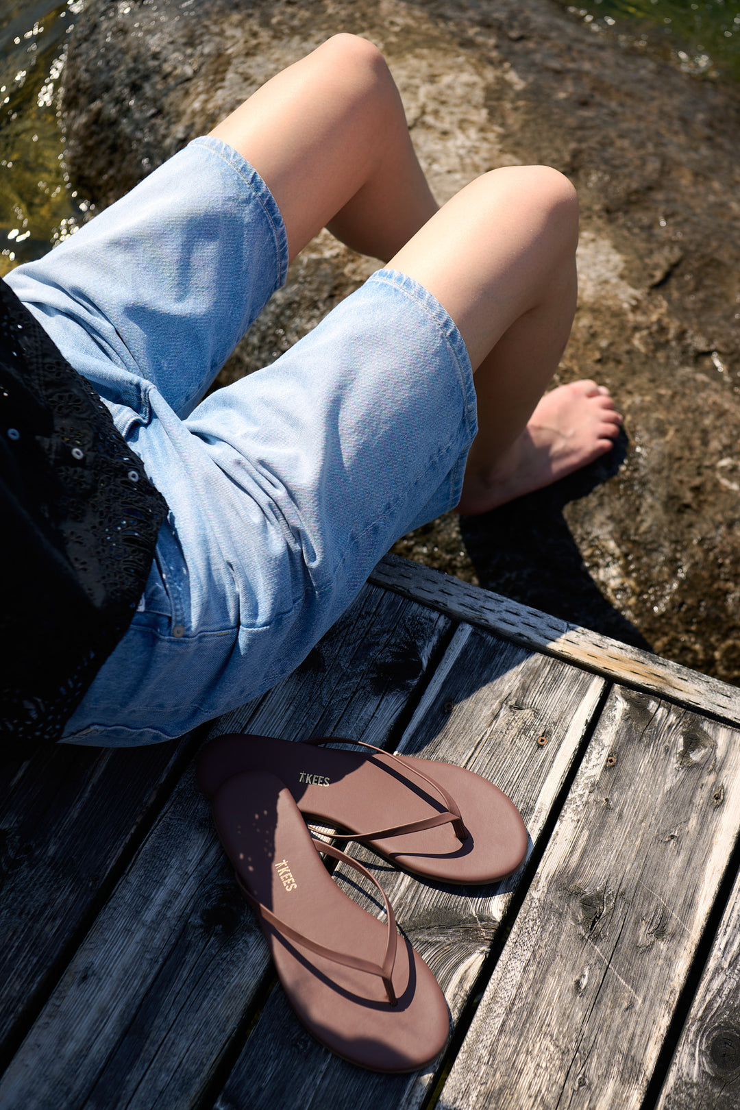 Barefoot denim-shorts detail with brown TKEES sandals resting on a Muskoka dock