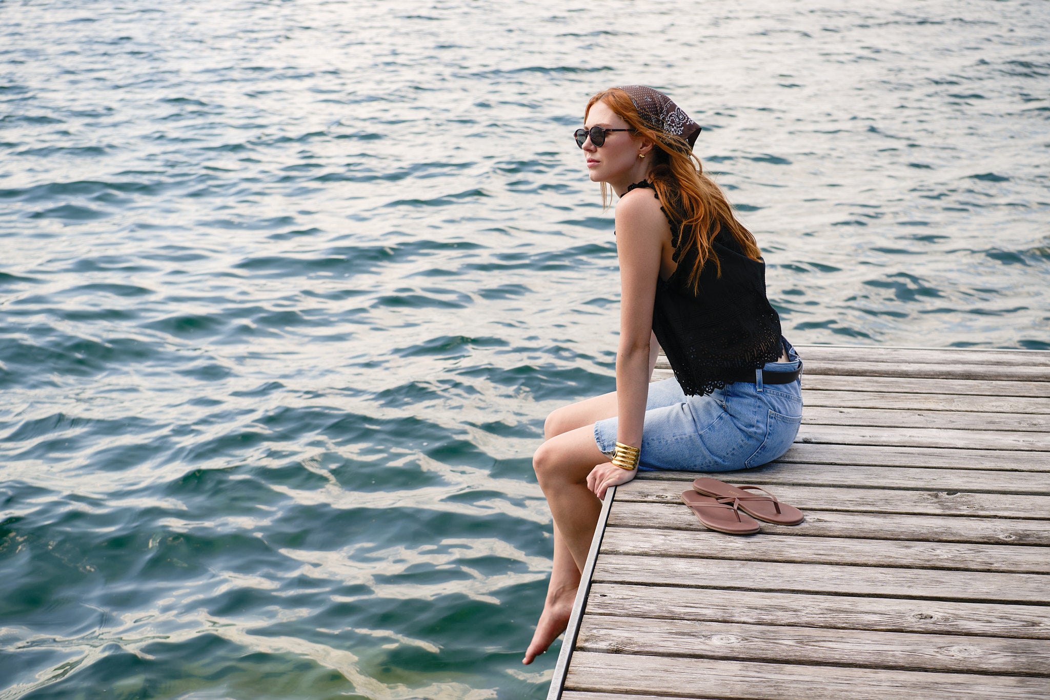 Wide dockside portrait of a model in a black DÔEN top and denim shorts beside the lake