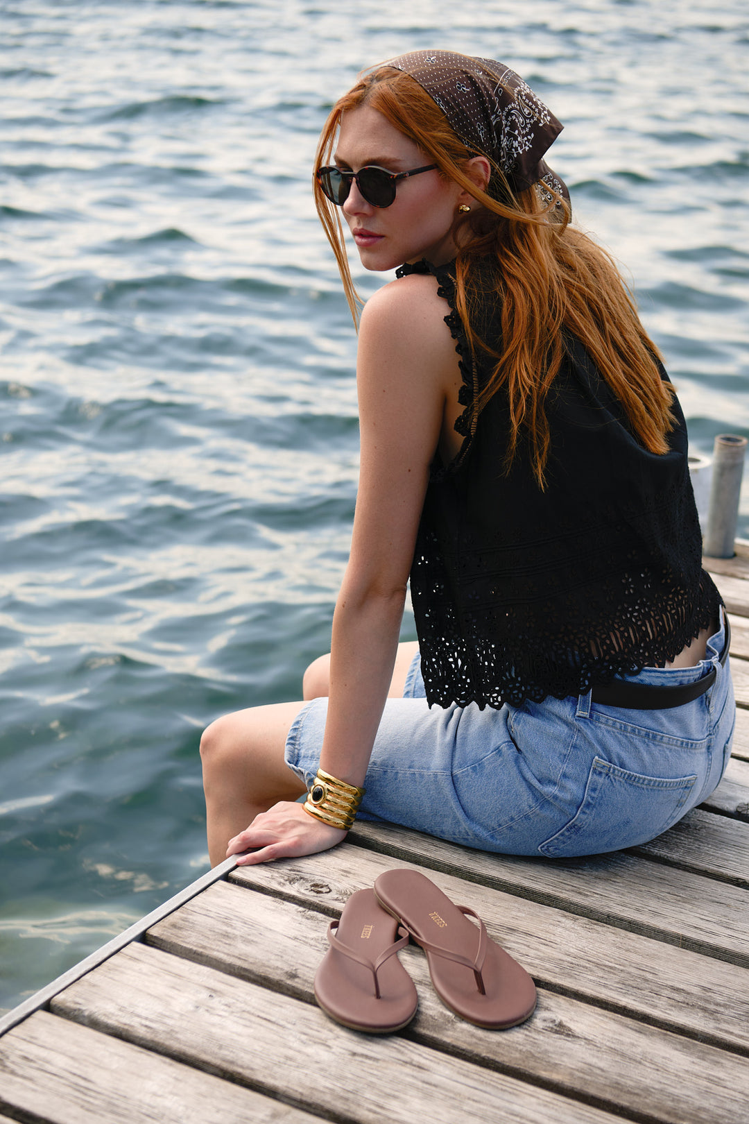 Rear three-quarter portrait in a black DÔEN top and AG Jeans shorts with sandals on the dock