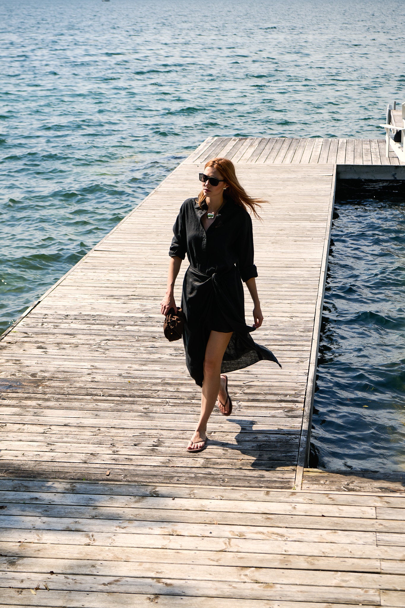 Model in a black Apiece Apart linen shirt dress walking a Muskoka dock for ANDREWS