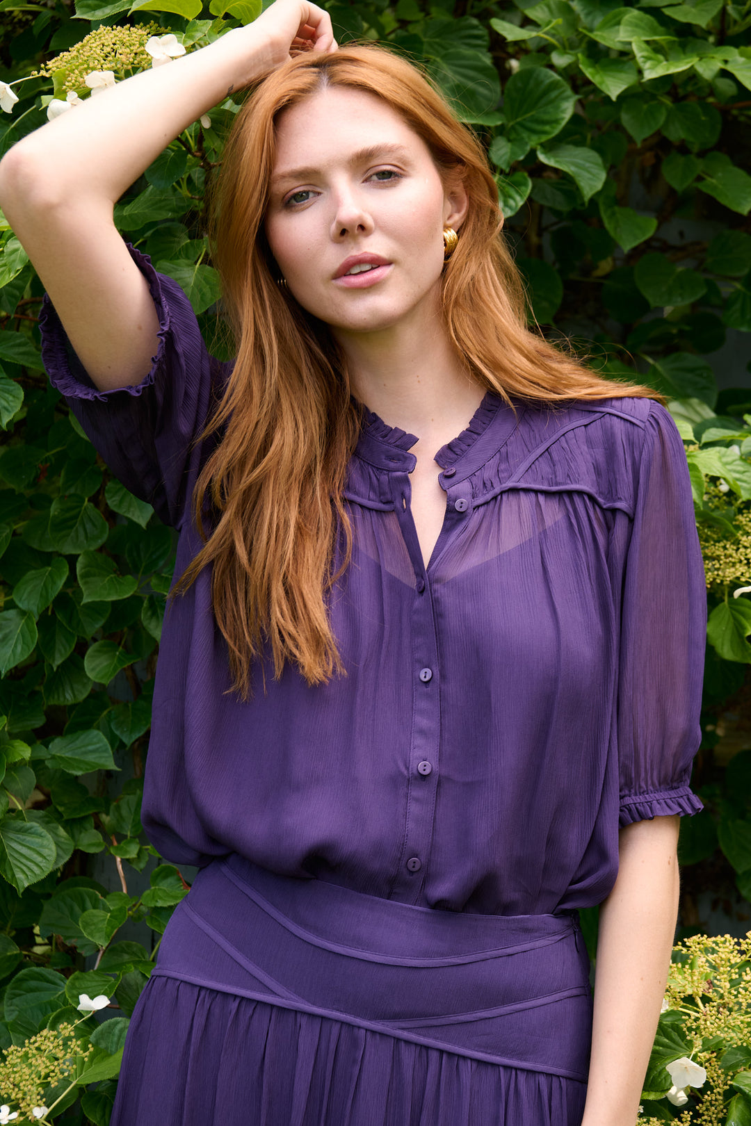 Close garden portrait of a model in a plum ba&sh blouse and skirt with gold earrings