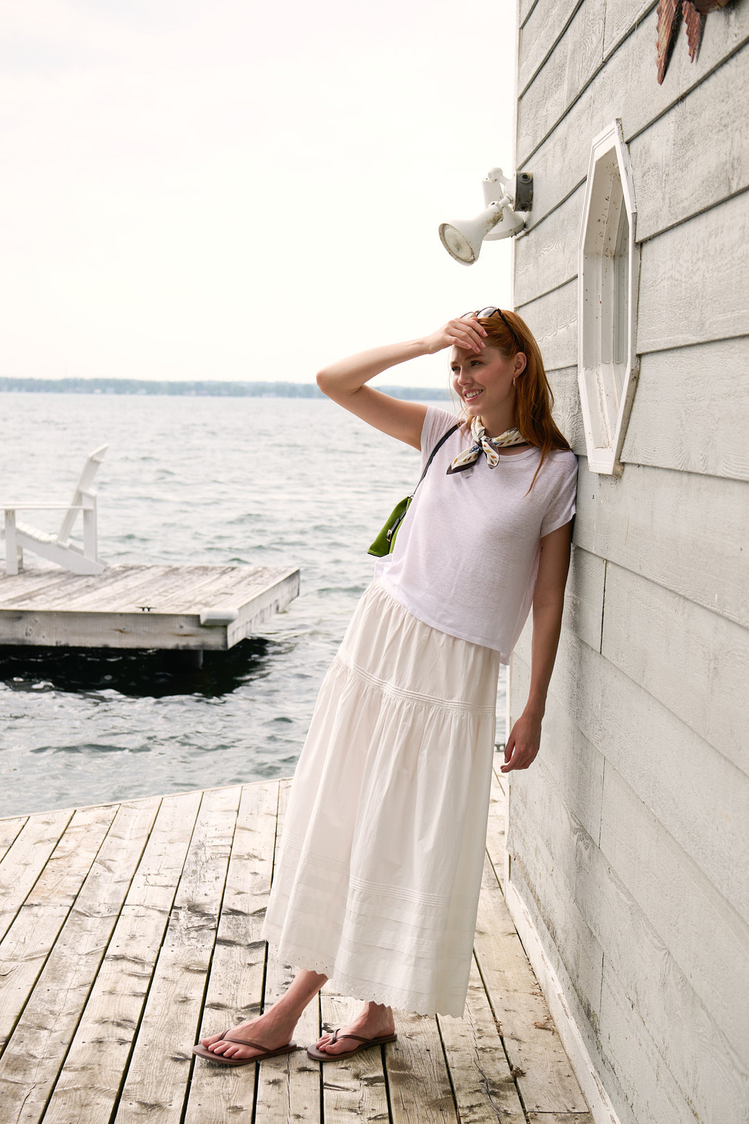 Model in a white Velvet tee and DÔEN skirt wearing a Longchamp silk scarf beside the boathouse