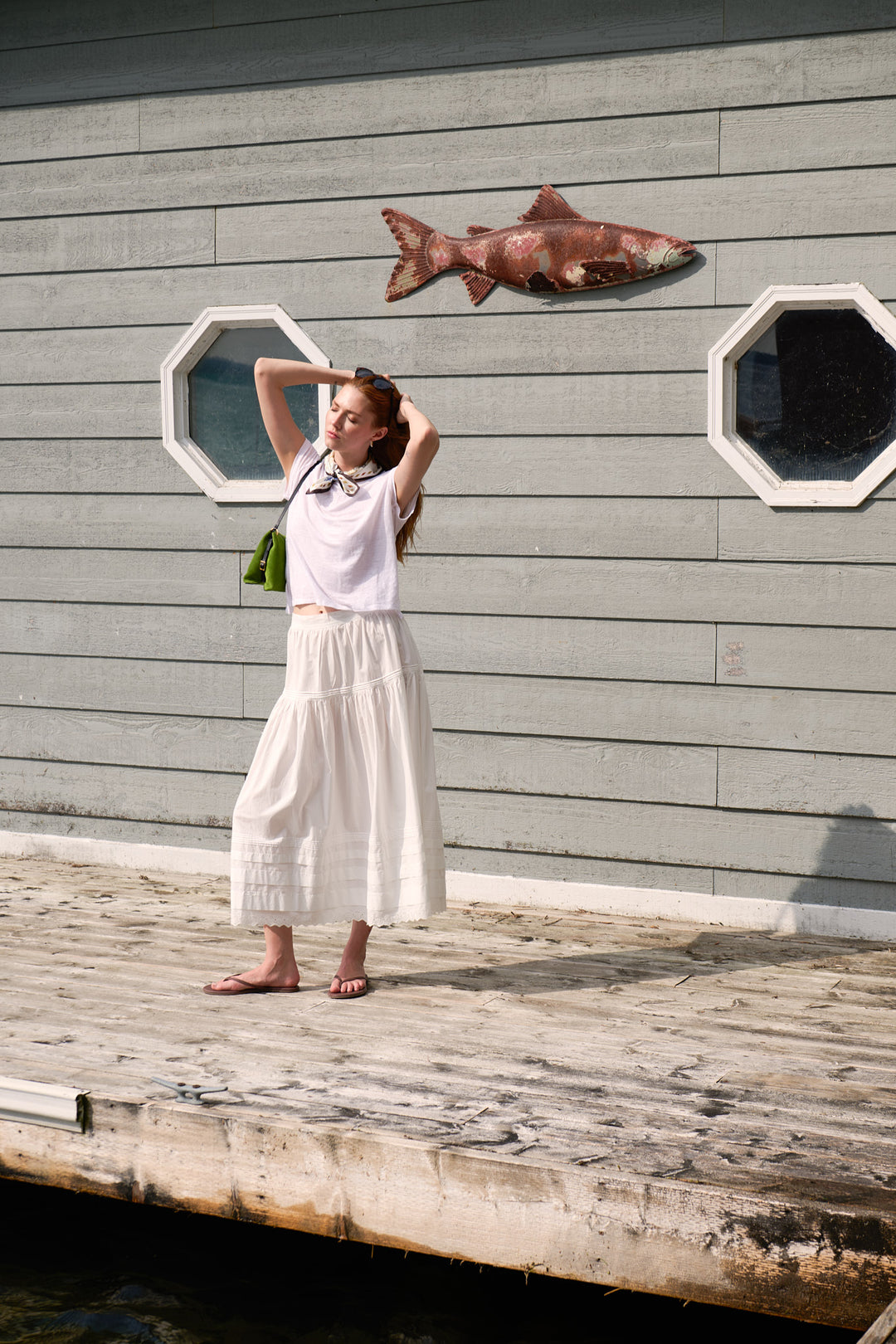 Model in a white Velvet tee and DÔEN skirt wearing a Longchamp silk scarf beside the boathouse