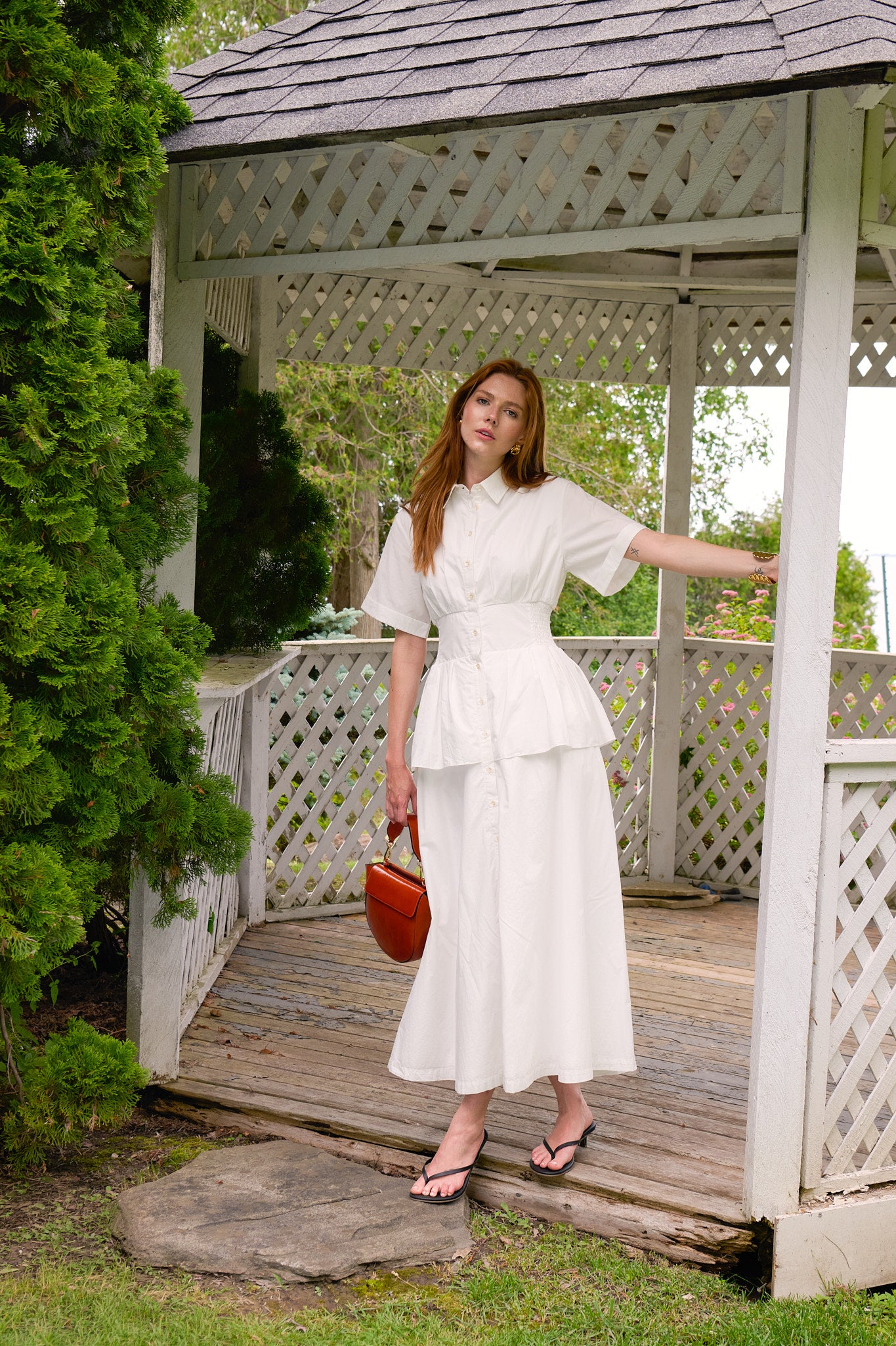 Rosie Assoulin white shirt dress styled with a cognac Wandler bag in a garden gazebo