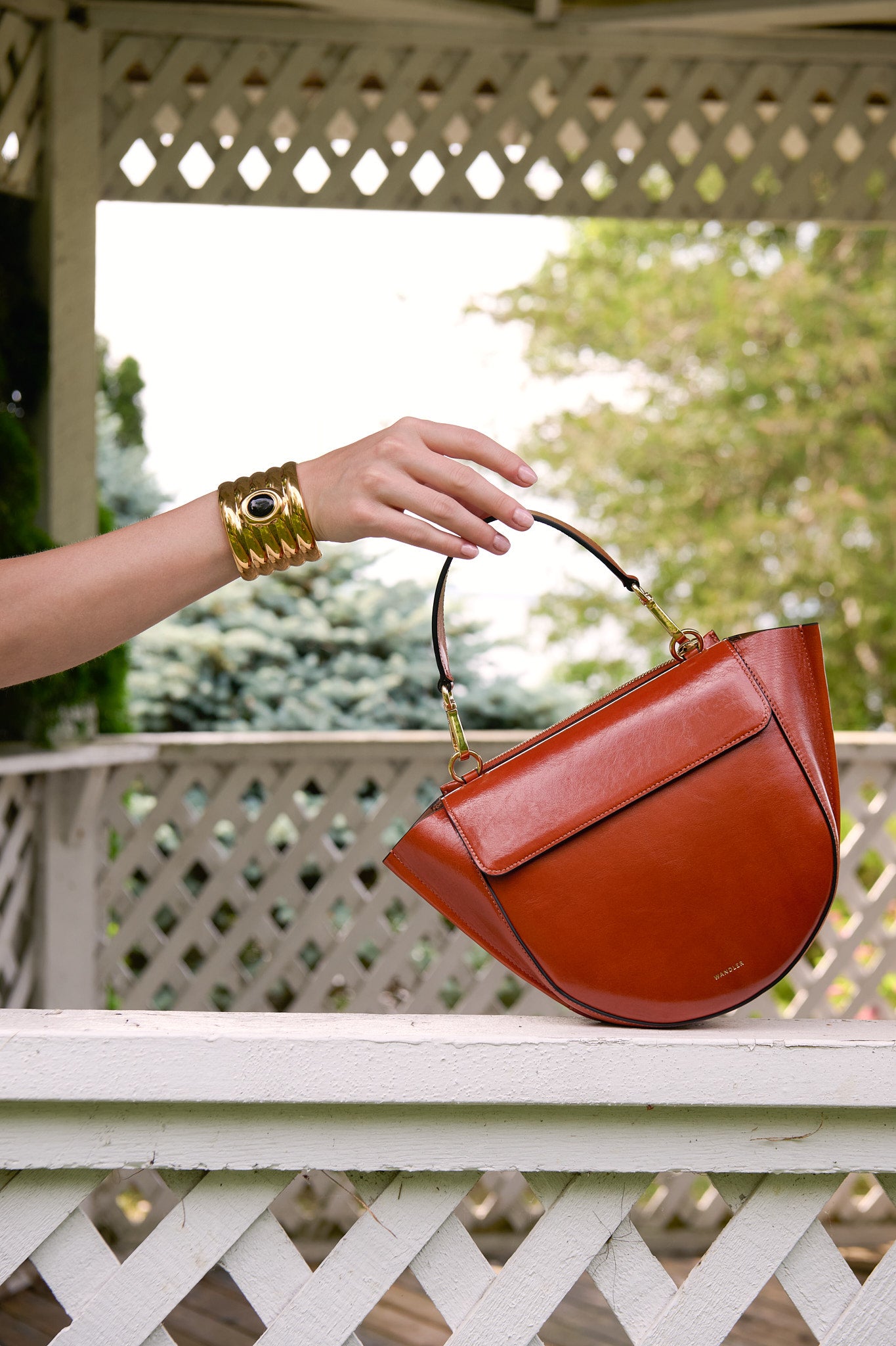 Wandler handbag and sculptural gold cuff by Heaven Mayhem displayed against white gazebo