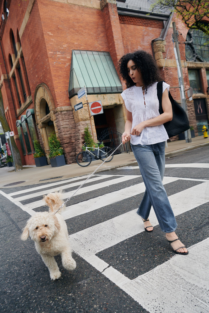 A woman walks her dog while wearing the The Gabby Embroidered Top by rag & bone and The Dodger Ankle jean by MOTHER, styled with The Nomad Hobo Bag by Naghedi