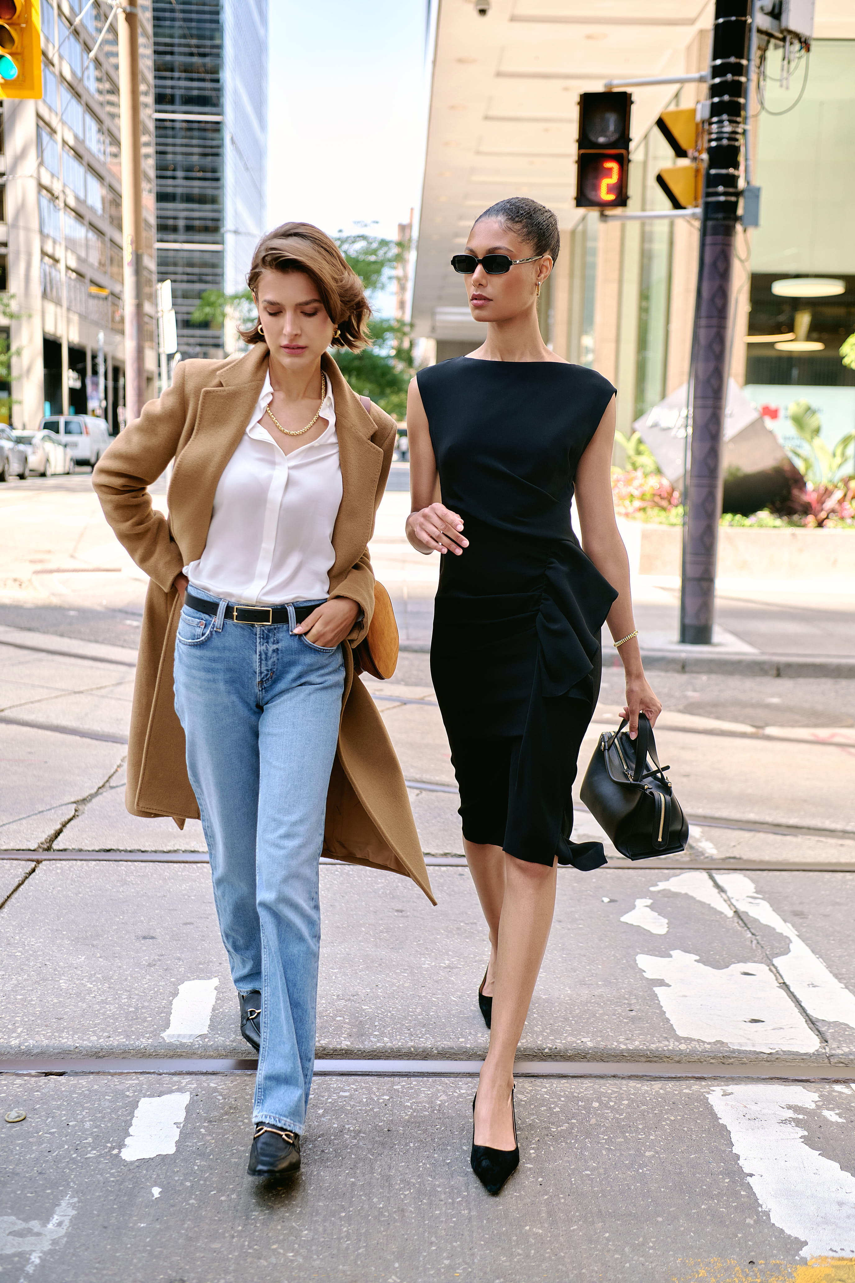 Two Models pose for Andrews Shops at First Canadian Place. One wears a Tagliatore coat, Agolde jeans, and a button-up shirt from Patrick Assaraf. The other wears a Max Mara dress with a Wandler handbag and shoes from Dear Frances
