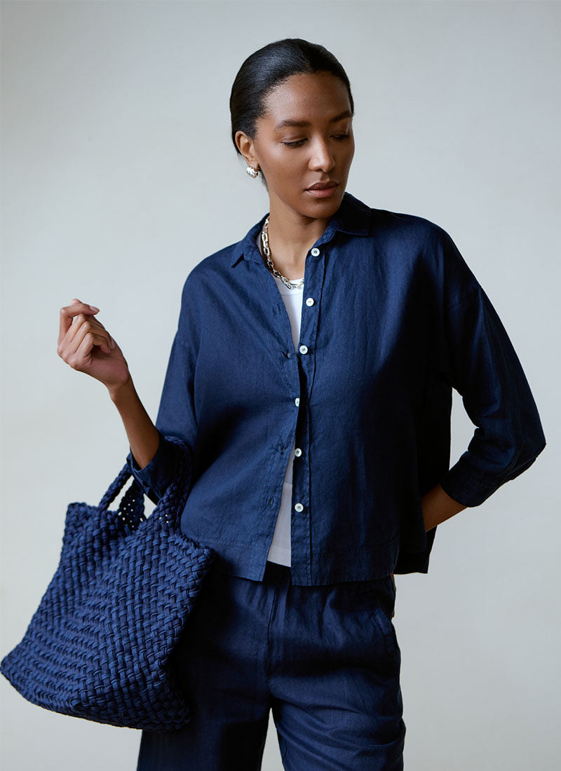 Woman wearing a navy blue shirt and pants holding a matching navy bag against a plain background