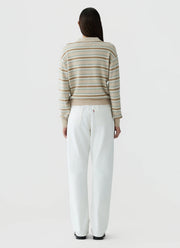 A woman viewed from behind wearing a beige and white striped knit sweater and white wide-leg trousers, standing against a light gray studio background.