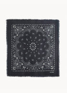 A square black bandana with white printed paisley and floral motifs, finished with fringed edges, shown flat against a light gray background. The brand name 'KUXTEN' is printed in small white letters in the bottom right corner.