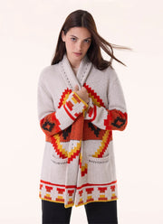 A woman modeling a light gray knit cardigan with a bold Southwestern geometric pattern in red, orange, yellow, and black, set against a plain off-white background.